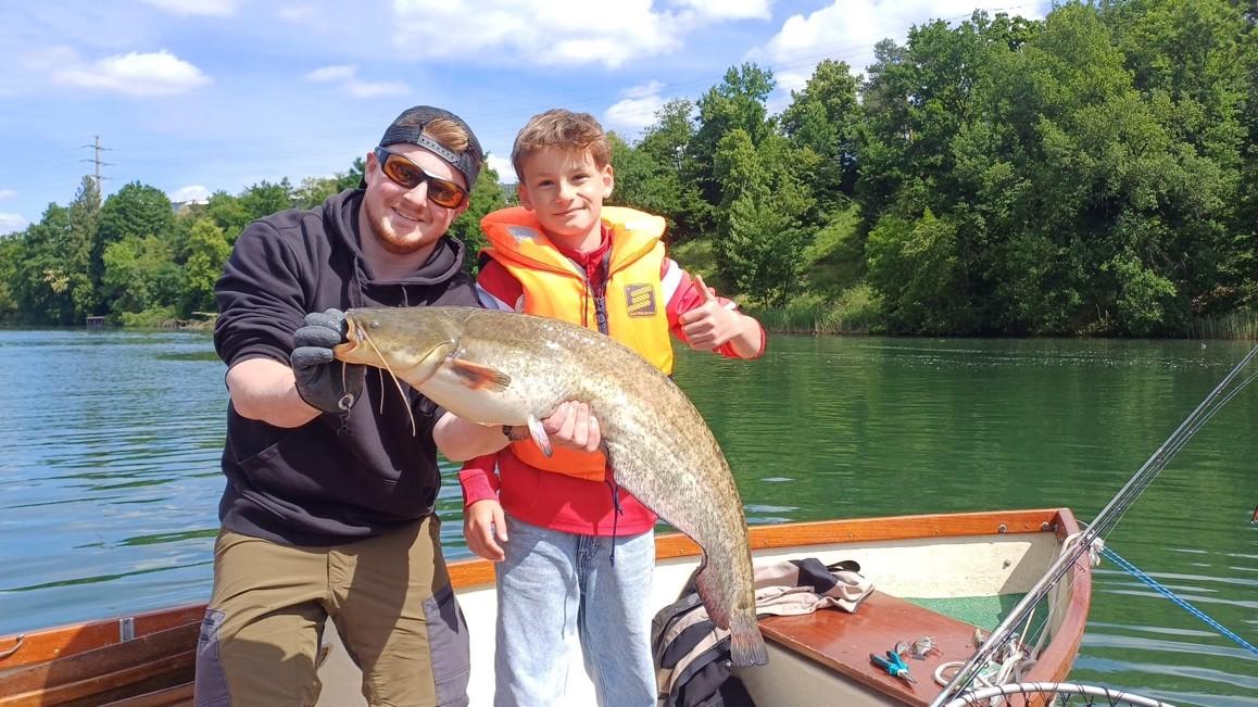 Wels, welcher von einem Jungfischer und dem Leiter gehalten wird